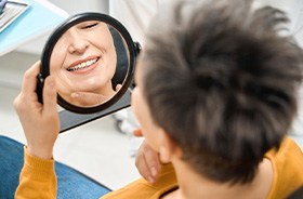 Smiling senior patient looking at her dentures in mirror